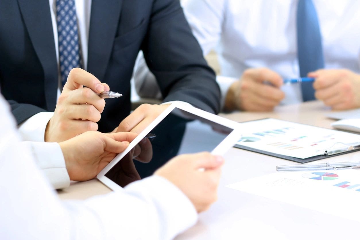 A group of people sitting at a table with papers and a tablet.