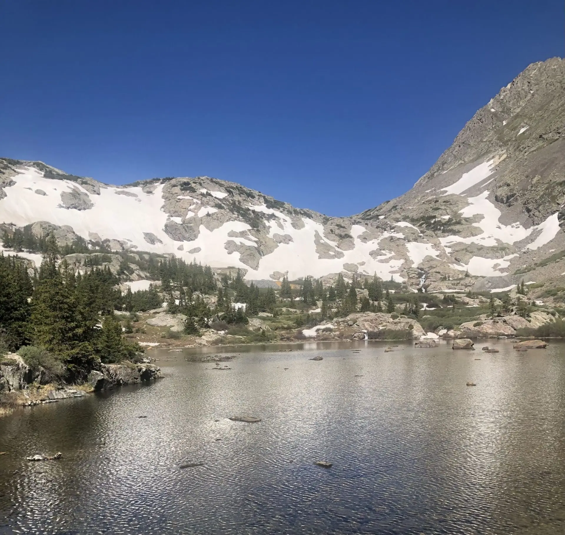 A lake with snow on the side of it and trees in front.